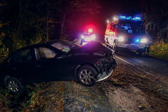 Image of a severe car accident at night with flashing police and ambulance lights, broken vehicles on a dark road, and emergency responders attending to the scene.